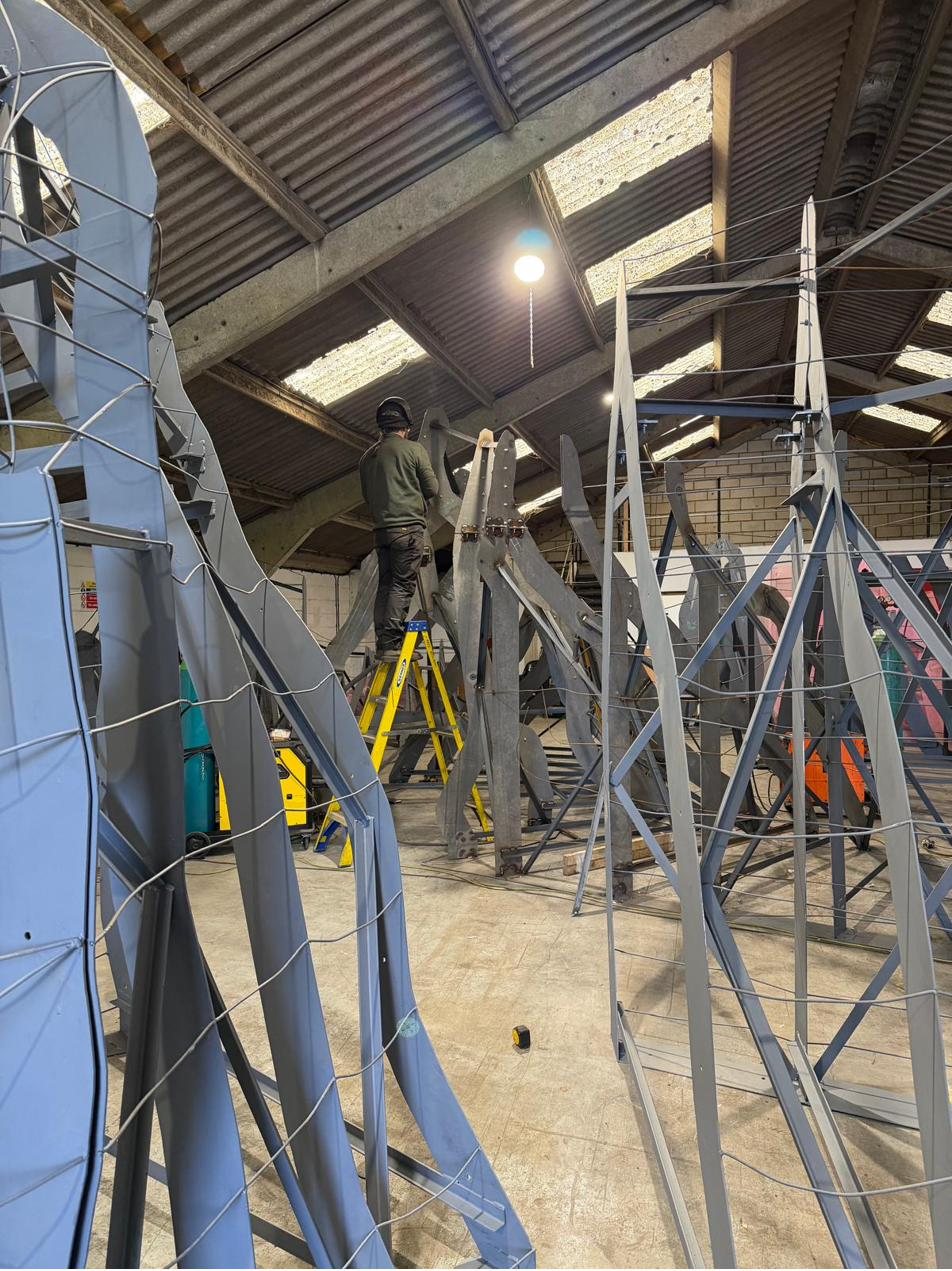 Tall welded steel armature ribs reaching towards the workshop roof