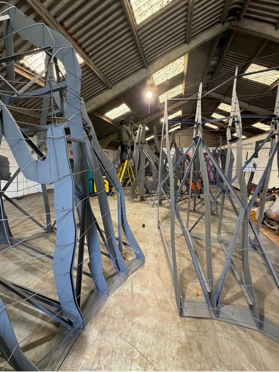 Rows of grey steel rib frames strung with wire lattice, a worker on a ladder behind