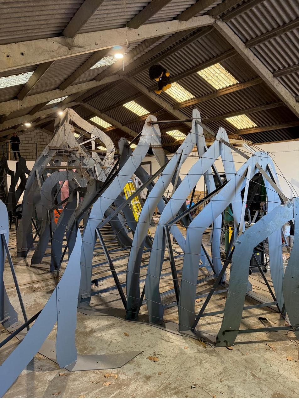 Bare welded steel armature ribs strung with wire lattice, standing in the workshop