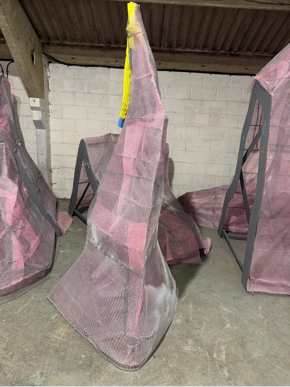Pink scrim-mesh forms on steel trestle stands in the workshop, ready for rendering