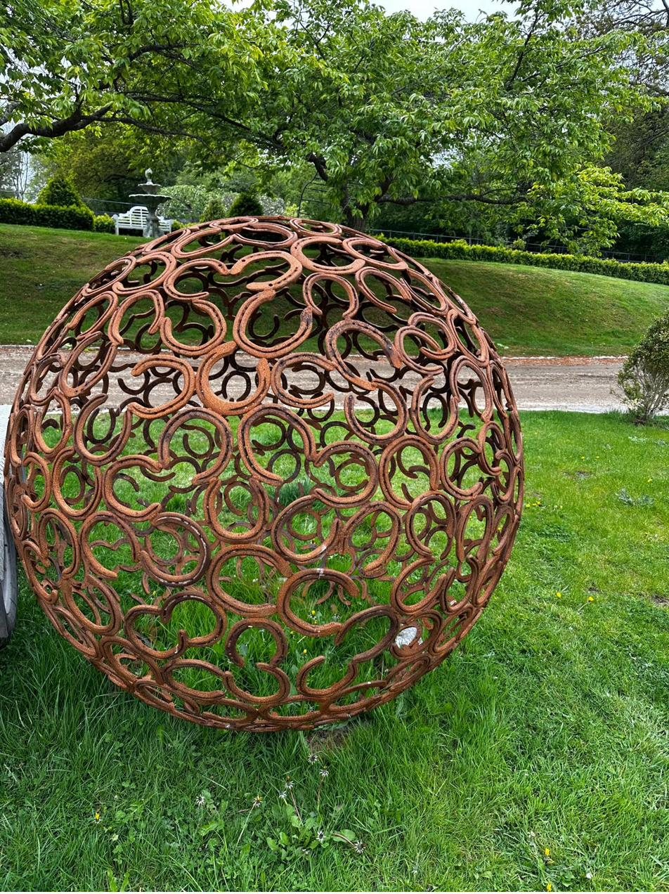 Forged steel sphere sculpture made from interlocking rings, in a garden setting