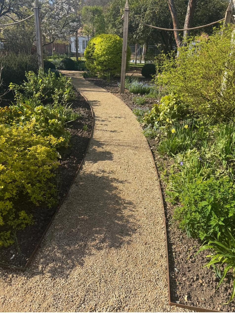 Curved gravel path with steel edging through planted borders
