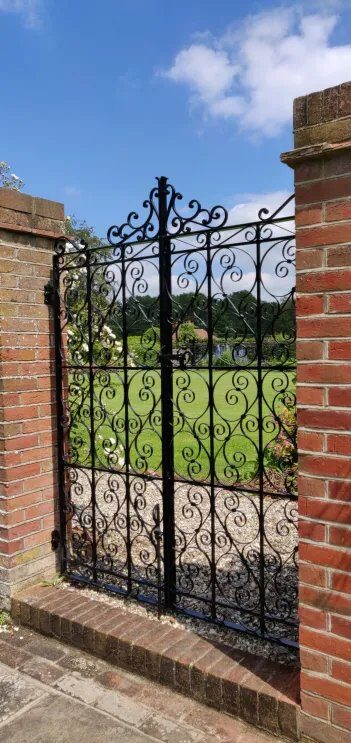 Tall ornate scrollwork garden gate with cresting and curlwork