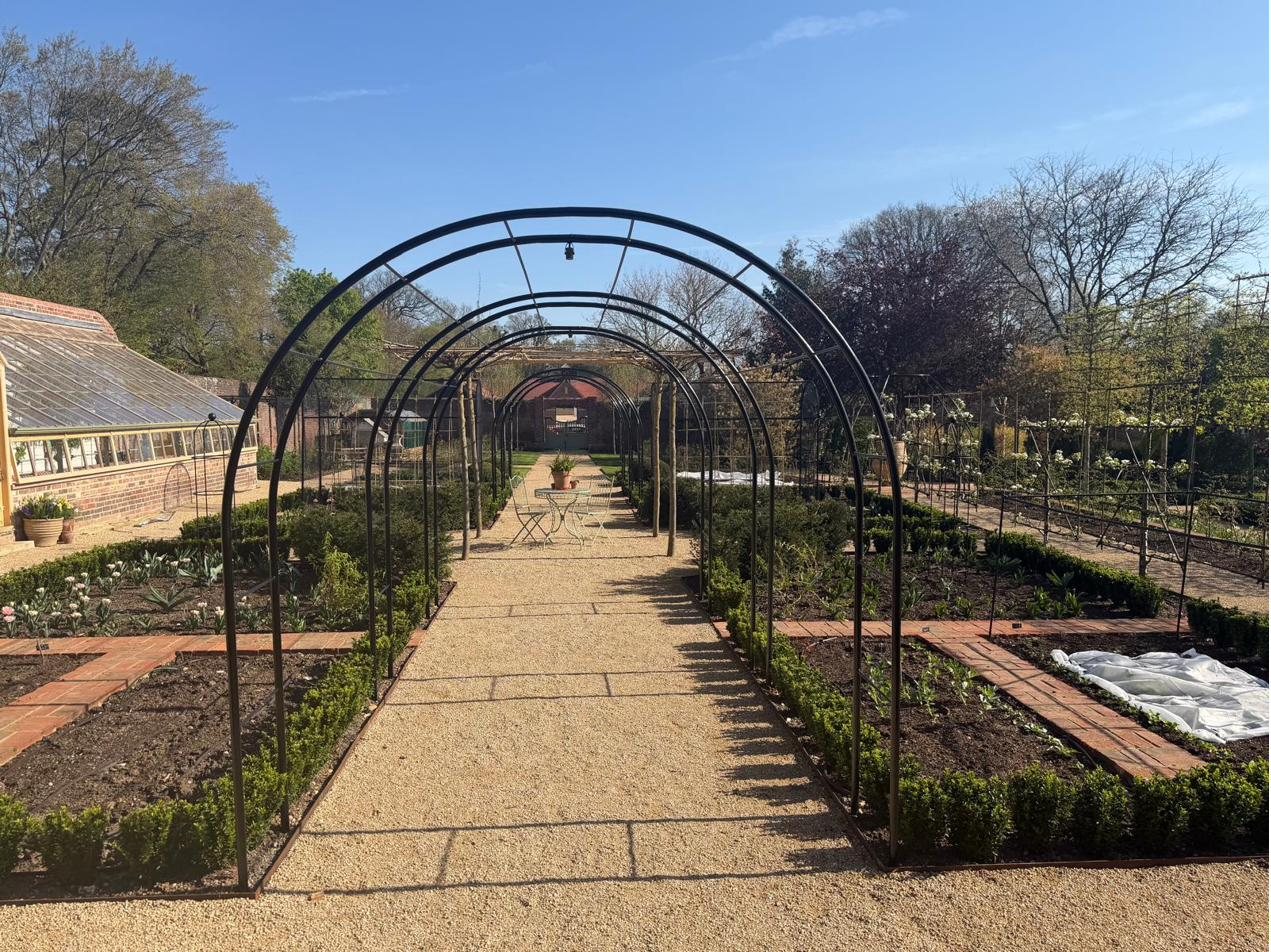 Long steel pergola archway walkway over a formal garden path