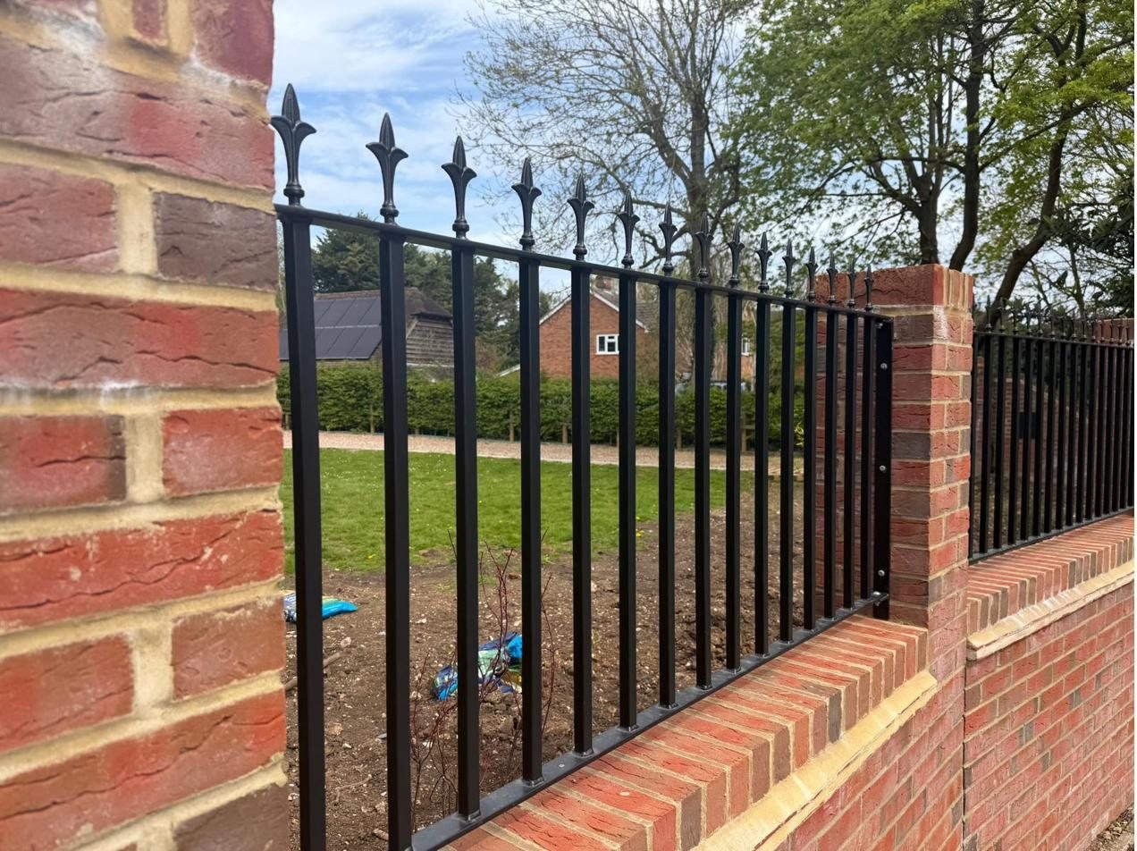 Spear-top boundary railings on a brick wall overlooking a lawn