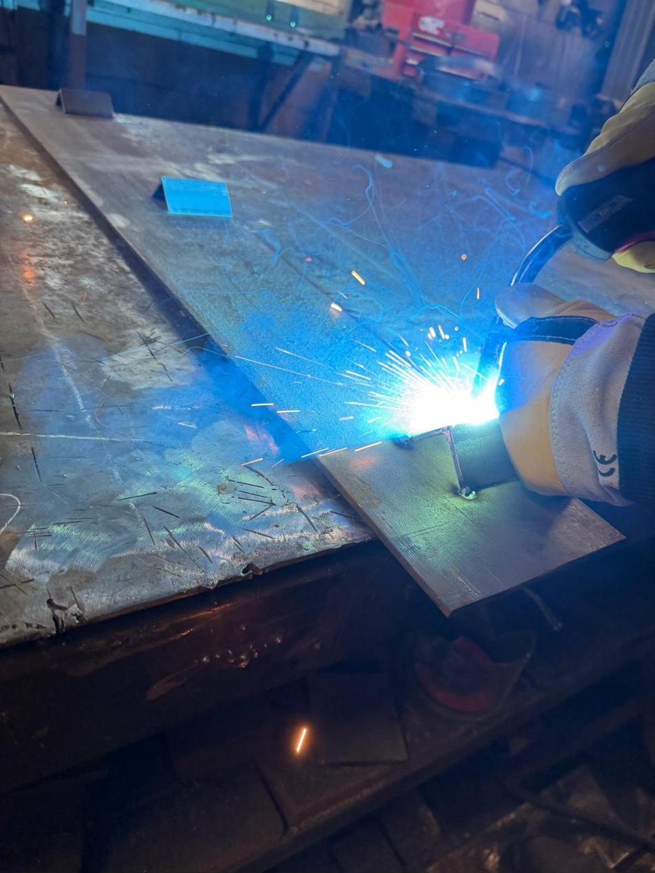 Close-up of a bright weld arc running along a steel plate on the bench